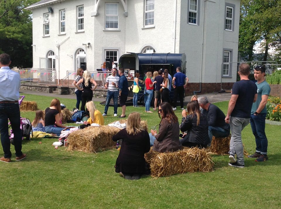 Families sitting on hay bales listening to band at community fun day at private school in Porthcawl, South Wales