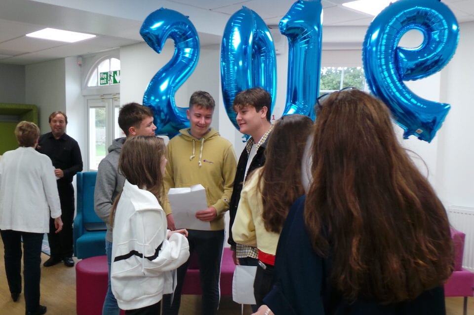 GCSE students stand beneath blue helium balloons spelling out 2019
